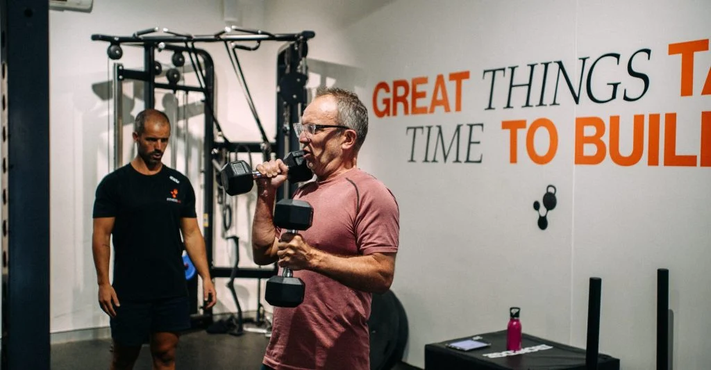 A coach watches a client holding a dumbbell in a FitnessLab studio.